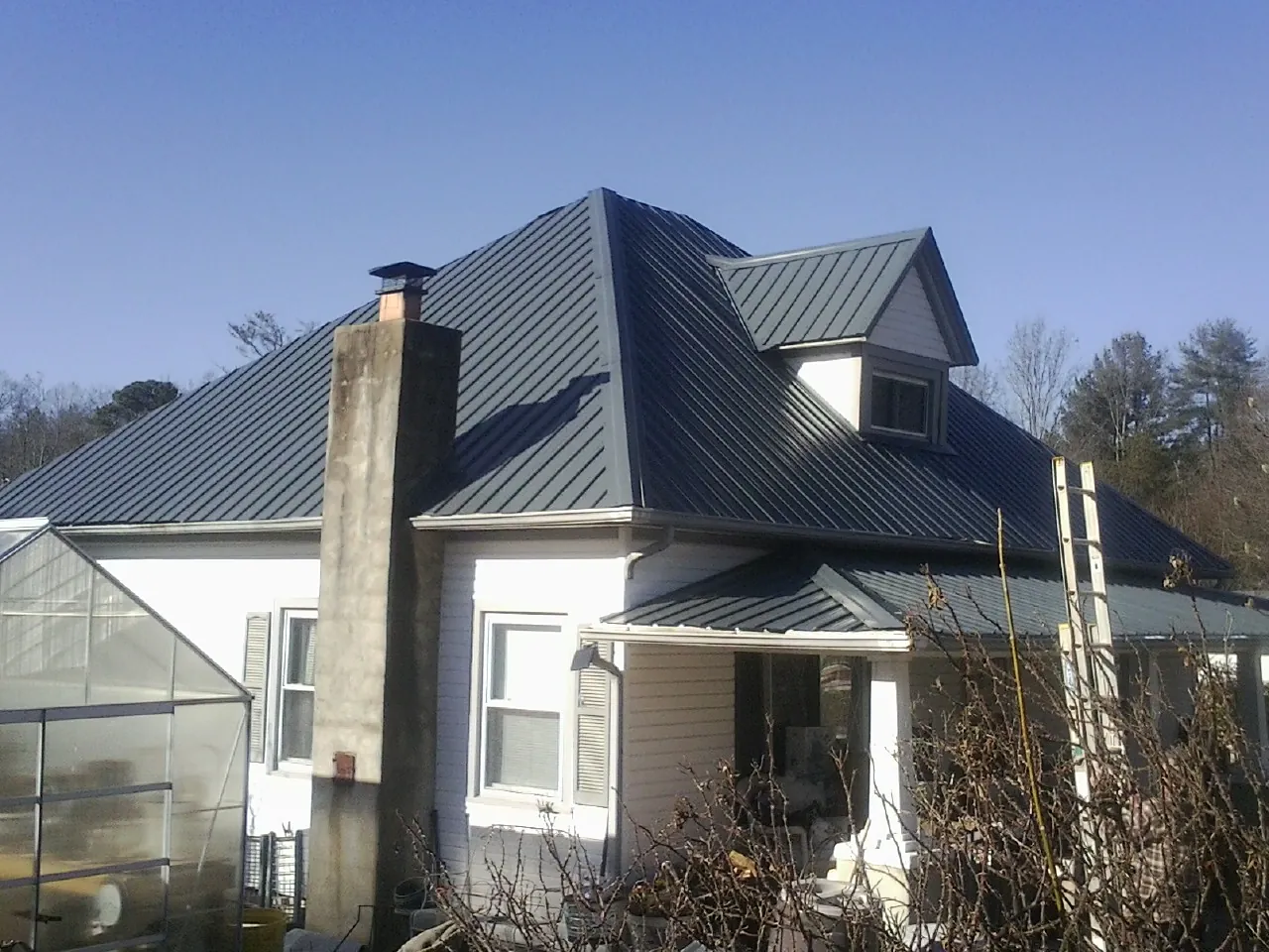 Dark blue standing seam metal roof on a white farmhouse with dormer — Slate & Tile Roof Repair by Roofing Brothers in Hankinson