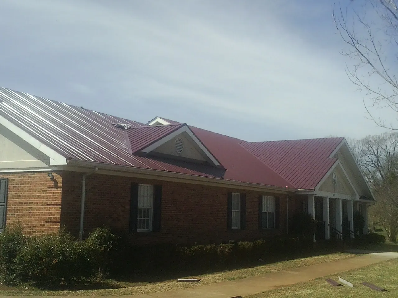 Red metal roof with gabled entries on a long brick building, from a Hail Damage Roof Repair job in Hankinson