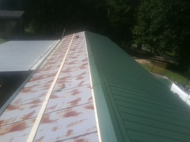 Old rusted panels beside newly installed green metal roofing — Wind Damage Roof Repair by Roofing Brothers in Hankinson