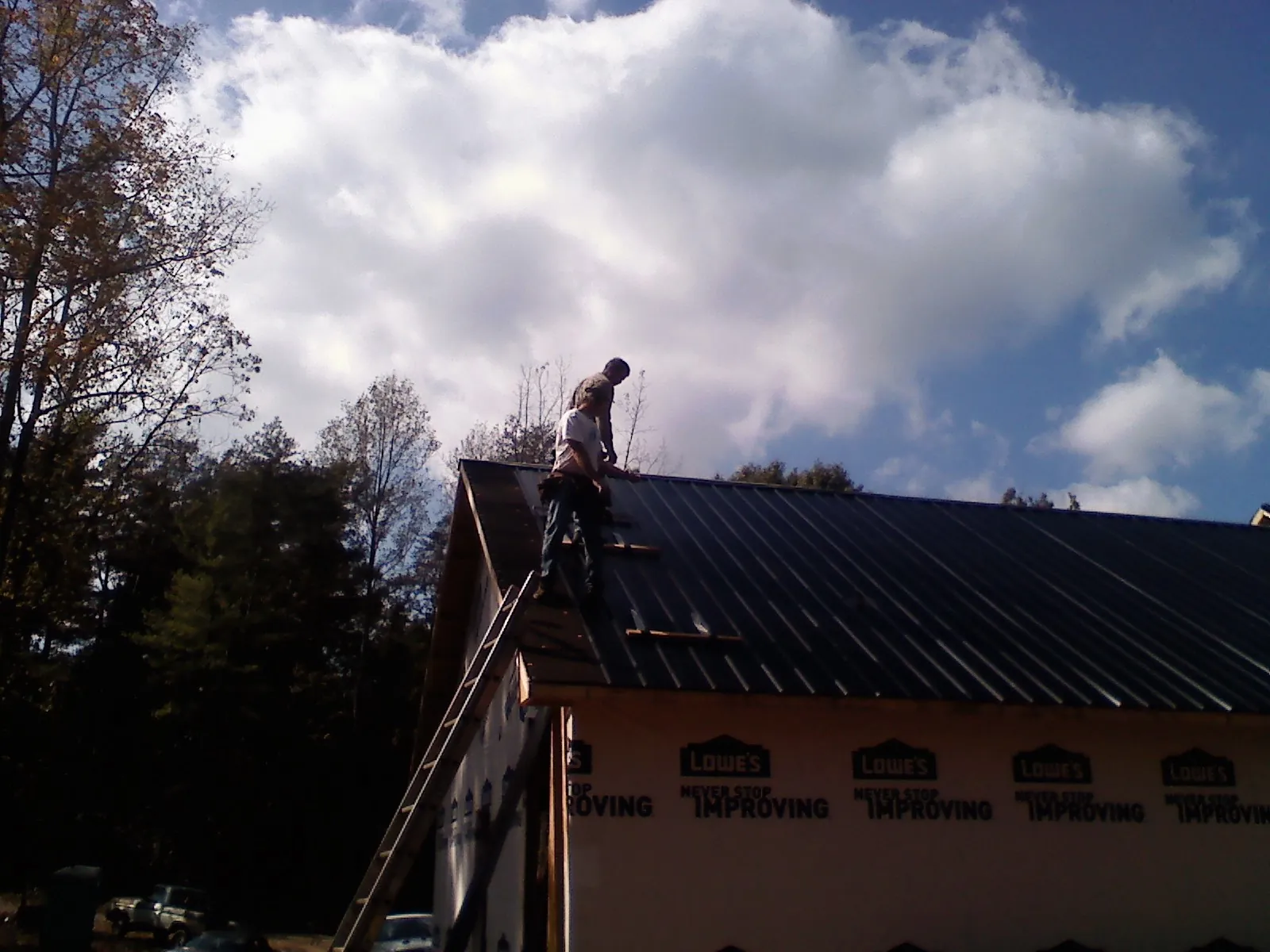 Roofer fastening dark metal panels high against a cloudy sky, from a Roof Inspection job in Hankinson
