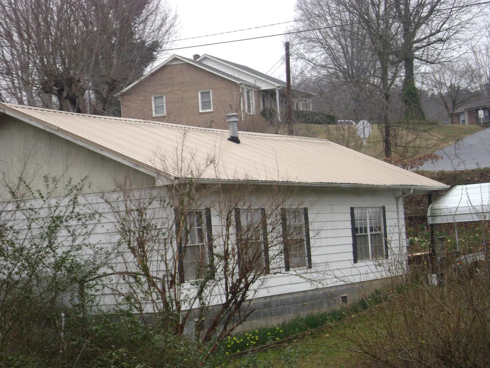 Tan metal roof on a white sided house set into a hillside — Commercial Roofing by Roofing Brothers in Hankinson